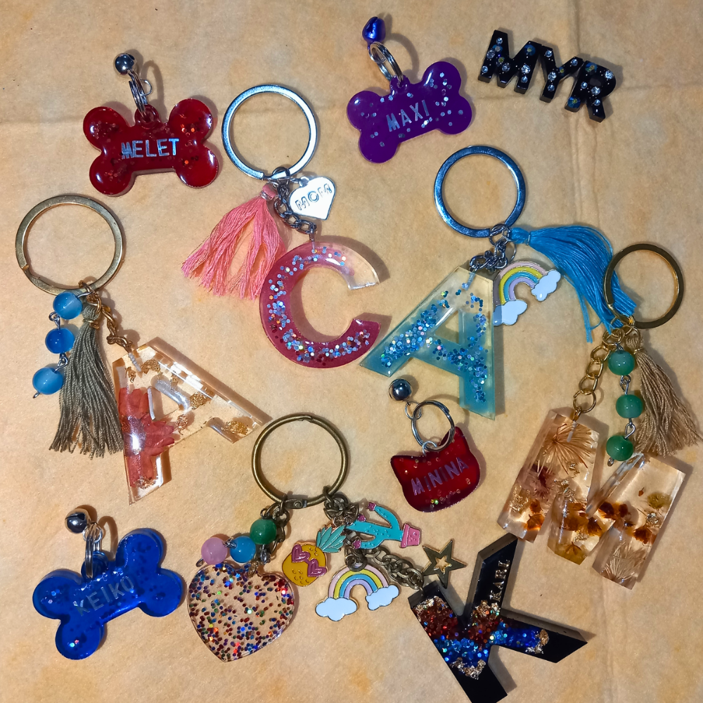 Chaveiros de resina personalizados em formato de letras e ossos, coloridos com glitter e miçangas.